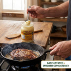 Hand spooning solid beef tallow into a hot skillet with a steak, batch tested for smooth consistency